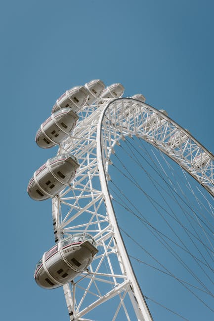 A close-up view of a large Ferris wheel against a clear blue sky, showing the white metal framework and multiple enclosed passenger cabins with windows. The Ferris wheel's structure appears clean and well-maintained, with no visible dirt or damage. The cabins are evenly spaced along the circular rim, and the overall scene conveys a sense of amusement park entertainment. This image is associated with the deep cleaning and surface maintenance services offered by Deep Cleaning Lambeth in relation to domestic and commercial cleaning needs.